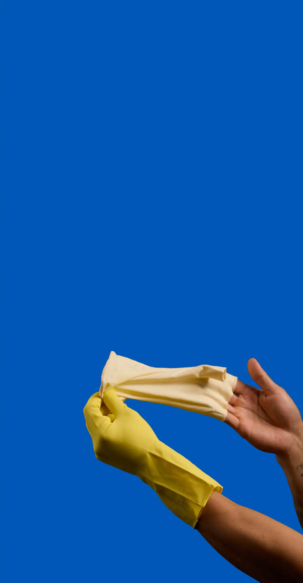 Hands wearing yellow gloves hold a folded white cloth against a bright blue background.